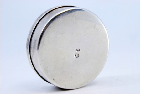  Caixa de comprimidos em prata lisa de forma circular com tampa amovível.